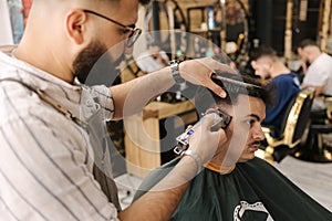 Handsome bearded man cutting hair of confident male client in berber shop