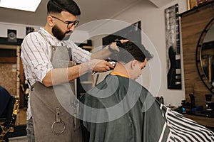 Handsome bearded man cutting hair of confident male client in berber shop