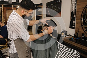 Handsome bearded man cutting hair of confident male client in berber shop