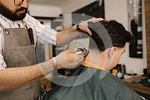 Handsome bearded man cutting hair of confident male client in berber shop