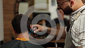 Handsome bearded man cutting hair of confident male client in berber shop