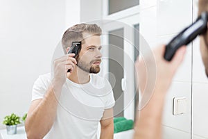 Handsome man cutting his own hair with a clipper