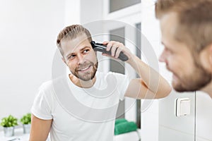 Handsome man cutting his own hair with a clipper