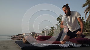 Handsome bearded man doing thai yoga massage for a woman at sunset seashore.