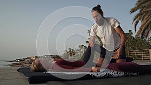 Handsome bearded man doing thai yoga massage for a woman at sunset seashore.