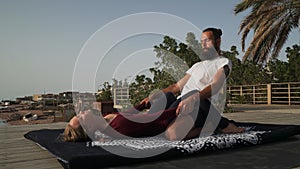 Handsome bearded man doing thai yoga massage for a woman at sunset seashore.