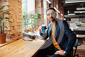 Handsome bearded man drinking coffee sitting near window