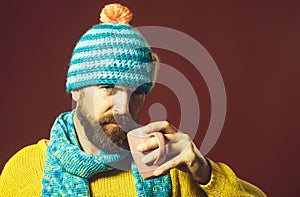 Handsome bearded man in fashionable clothes drinking beverage from cup. Serious stylish male in sweater and hat wrapped