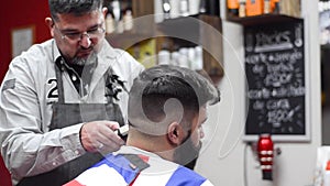 Handsome bearded man getting haircut by hairdresser at the barber shop.