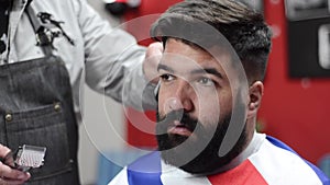 Handsome bearded man getting haircut by hairdresser at the barber shop.