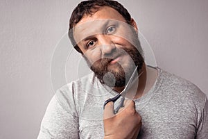 Handsome bearded man in gray t-shirt cutting his beard with scissors