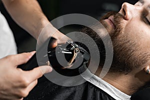 Handsome bearded man has hair and beard cut in barbershop. Dreadlock barber cuts client& x27;s hair