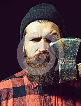 Handsome bearded man in hat holds axe on black background