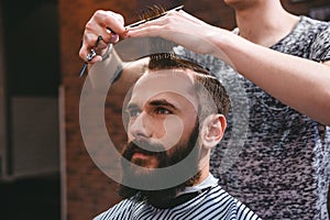 Handsome bearded man having haircut with comb and scissors