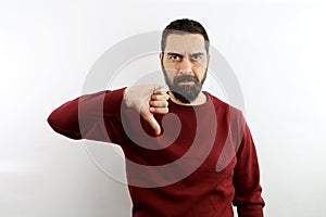 Handsome bearded man on isolated white background with casual shirt makes the thumbs-down hand sign.