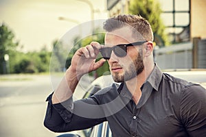Handsome bearded man next to car in sunglasses