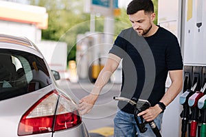 Handsome bearded man refueling car at self service gas station. Petrol concept