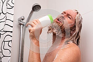 Handsome bearded man singing while taking shower using shampoo bottle instead of microphone