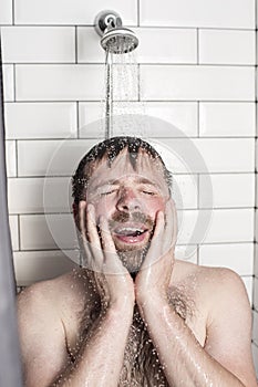 A handsome, bearded man stands in the shower under running water