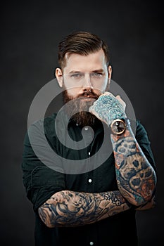 Handsome bearded man with tattoos on his hands looks at the camera with a thoughtful look