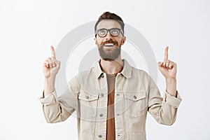 Handsome bearded man thanking god for good luck standing in beige casual jacket over gray background looking and