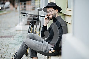 Handsome bearded man is using a smart phone and smiling while riding bicycle in city