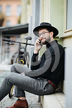 Handsome bearded man is using a smart phone and smiling while riding bicycle in city