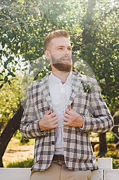 Handsome bearded man in vintage clothing. Portrait stylish groom in plaid jacket on his wedding day in the park. Rustic