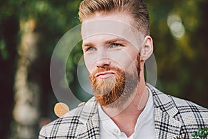 Handsome bearded man in vintage clothing. Portrait stylish groom in plaid jacket on his wedding day in the park. Rustic hipster