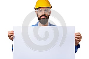 Handsome bearded man worker in protective helmet holding white advertising banner with copy space, isolated on white background