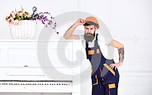 Handsome bearded mover posing next to retro piano isolated on white background. Small break from tiresome work