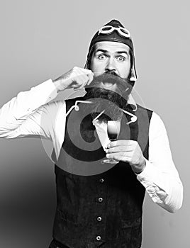Handsome bearded pilot or aviator man with long beard and mustache on funny face holding glass of alcoholic shot in