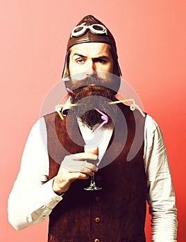 Handsome bearded pilot or aviator man with long beard and mustache on serious face holding glass of alcoholic shot in