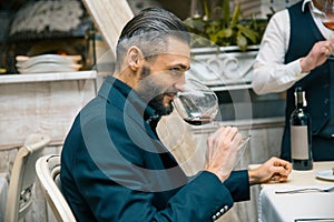 Handsome bearded rich man with stylish mustache and beard holding glass and sniff smell of red wine at the restautant.