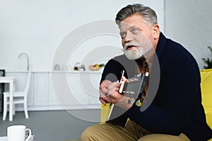 handsome bearded senior man playing guitar and looking away