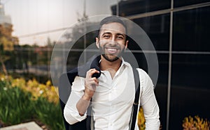 Handsome bearded smiling Indian businessman standing with jacket over shoulders