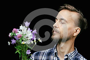 Handsome bearded stylish man looking on bouquet of tender wild flowers on black background. Gift for my love. Greeting card,