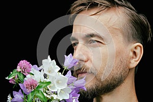 Handsome bearded stylish man sniffs aroma of tender wild flowers on black background. Gift for my love. Feeling nature