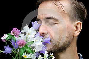 Handsome bearded stylish man sniffs aroma of wild flowers on black background. Gift for my love. Feeling nature concept