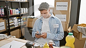 Handsome bearded young caucasian man volunteering at a local charity center, focused on his smartphone as he types out messages