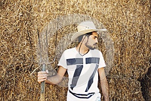 Handsome bearded young cowboy holding a pitch fork.