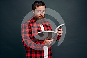 Handsome bearded young man in checkered shirt reading book isolated on a grey background