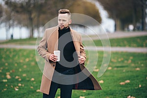 Handsome bearded young man in sunglasses drinking coffee in park, copy space on cup