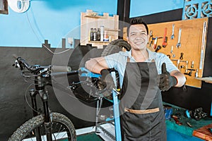 handsome bicycle mechanic in apron smiling wearing gloves and holding socket wrench with thumbs up