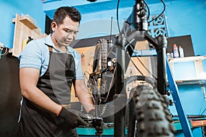 Handsome bicycle mechanic in an apron wearing gloves when installing bicycle pedals