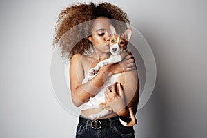 Handsome black african female with afro hair hugging and kissing her puppy basenji dog. Love between dog and owner. On