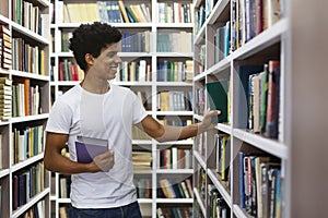 Handsome black guy looking for book on bookshelves in library