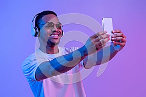 Handsome Black Guy In Wireless Headphones And Sunglasses Taking Selfie On Smartphone
