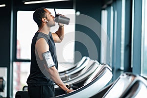 Handsome Black Male Athlete Drinking Water While Training At Treadmill At Gym