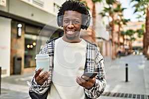 Handsome black man with afro hair wearing headphones listening to music using smartphone